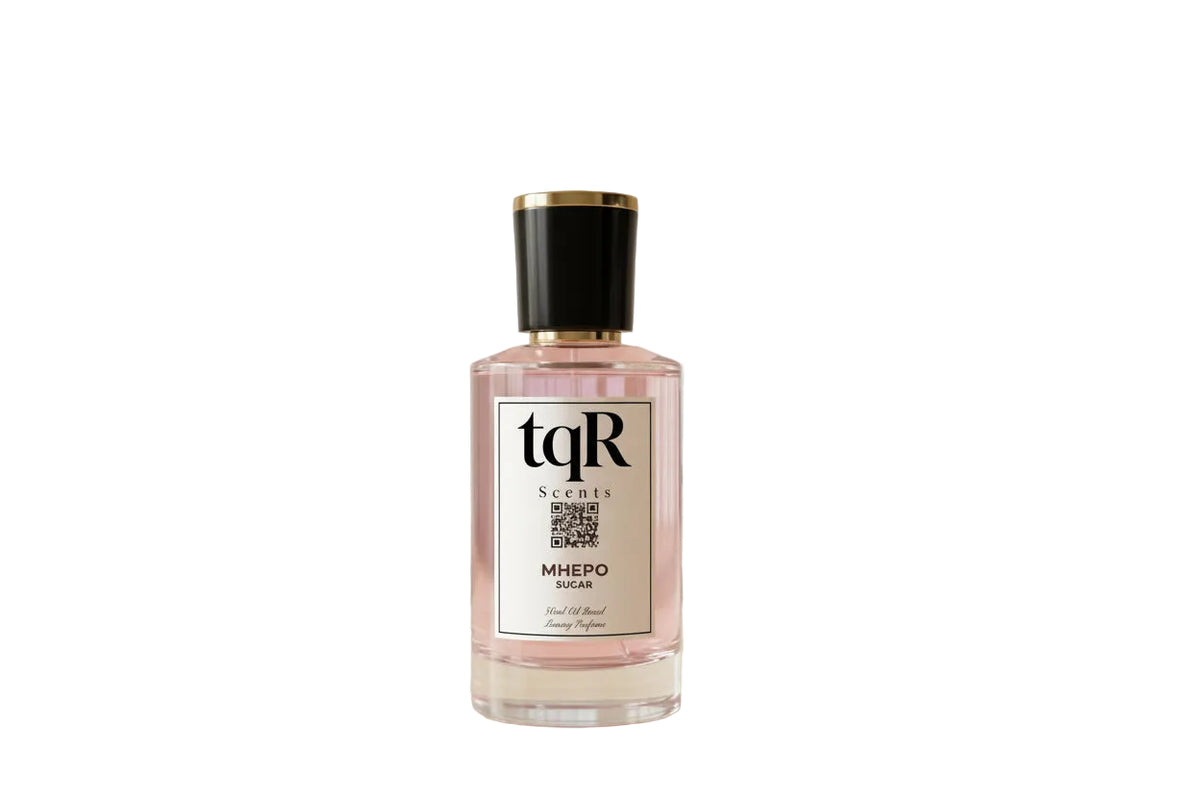 A bottle of tqR Scents Mhepo Sugar perfume stands on a light wood surface against a warm beige background, next to a printed fragrance notes card showing peach, coconut, lime, pineapple, banana, musk, ambergris, sandalwood, and scent profile notes.